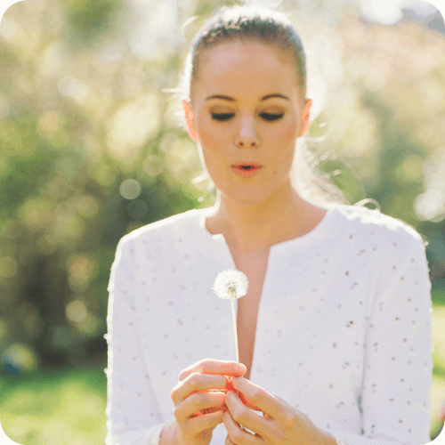 Femme heureuse et épanouie soufflant sur un pissenlit