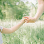 Enfant qui tend une fleur à sa maman dans un jardin