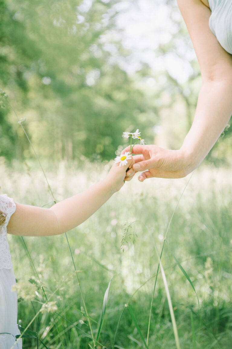 Enfant qui tend une fleur à sa maman dans un jardin